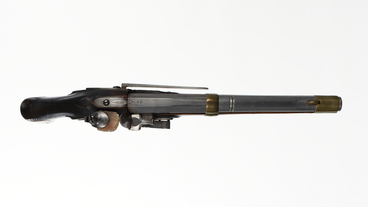 Pistol med flintlås, troligen förändringsmodell av år 1807 eller 1808. Stocken av trä, brun. Pipa och mekanism av stål. Beslagen av mässing. Kammarstycket 5-kantigt, märkt AH med krona över och därunder H och NT. På sidan GN.