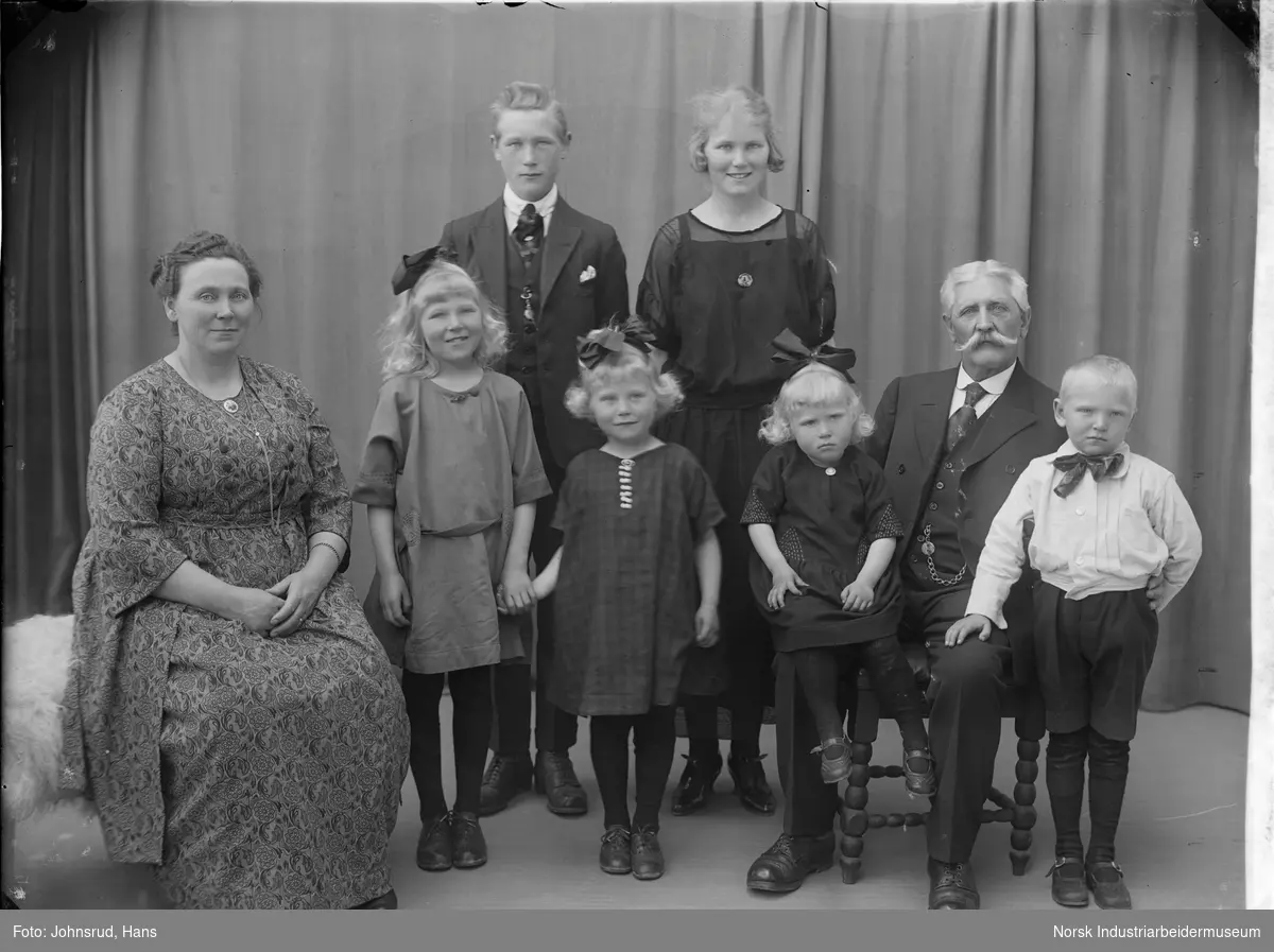 Vaktmester Bøe med kone og seks barn. Alle er kledd i pentøy og fotografert i studio.