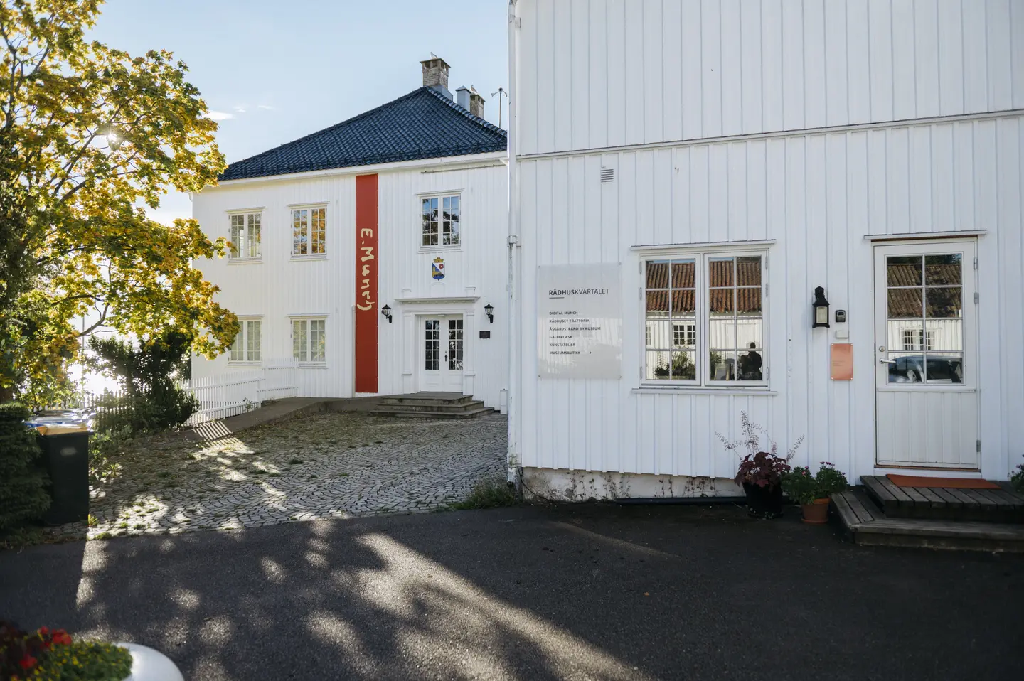 Foto av to hvite, eldre hus. Det ene huset har en lang vertikal banner i rød farge. På banneren står det Munch