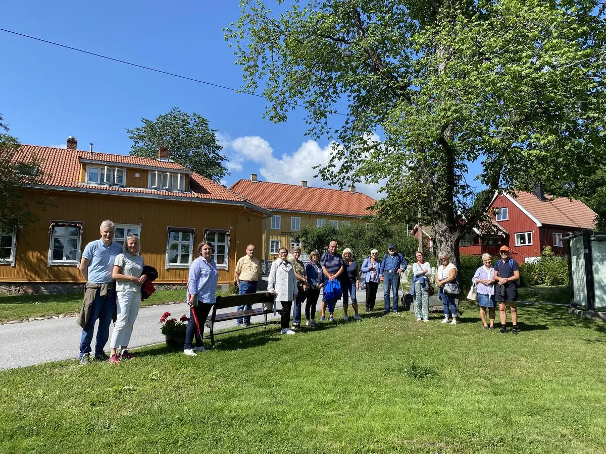 En gruppe mennesker på en gressplen foran eldre trehusbebyggelse.