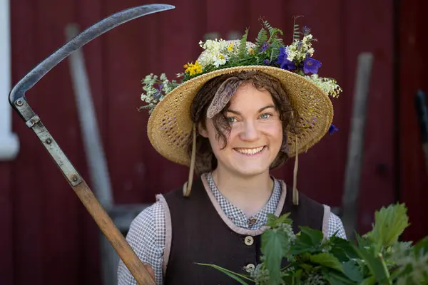 Kvinne med hatt, blomster og ljå.