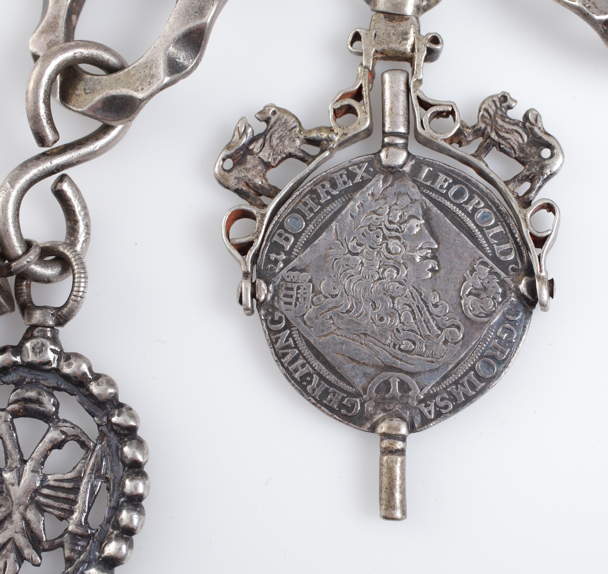 Chatelaine av silver. Kortare dekorerad kedja försedd med två urnycklar, signet (A.E.), amulett i filigranarbete och elfenben, vari antagligen suttit en bit av korall.

Äldre, österrikisk tillverkning.

Inskrivet i huvudkatalog 1909.