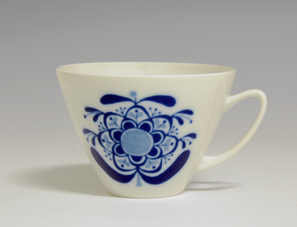 Kopp av porselen med hvit glasur. Dekorert med blå i-glasurdekor.
Modell: Jubileum 2340, formgitt av Eystein Sandnes i 1959.
Dekor: Beth Breyen
