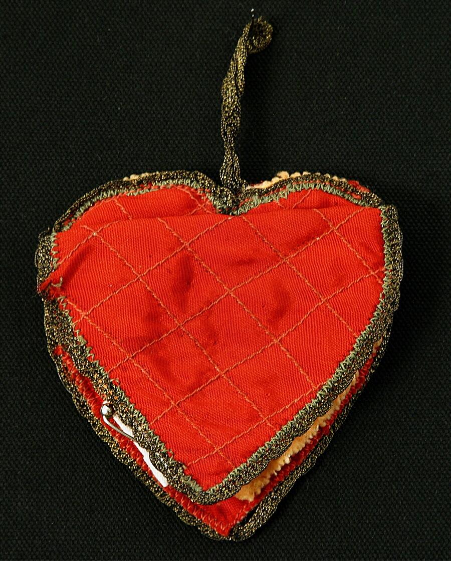 Nålbrev i forma av ett hjärta i rött (konst)siden, inuti ett "blad" av laxfärgad filt med flera nålar i. Framsidan matlasserad, kantad med mycket smal "metall"spets, försett med ögla.
Nyreg mars 2003 LJ