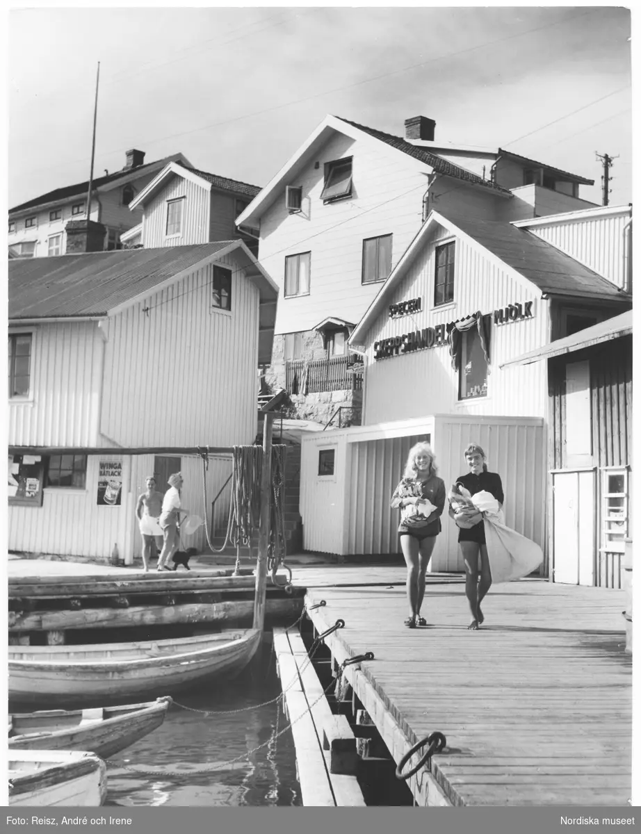 Bohuslän. Smögen, fiske- och badort på Västkusten. Två unga kvinnor på kajen utanför Skeppshandel / Speceri  med varsin kasse i famnen.