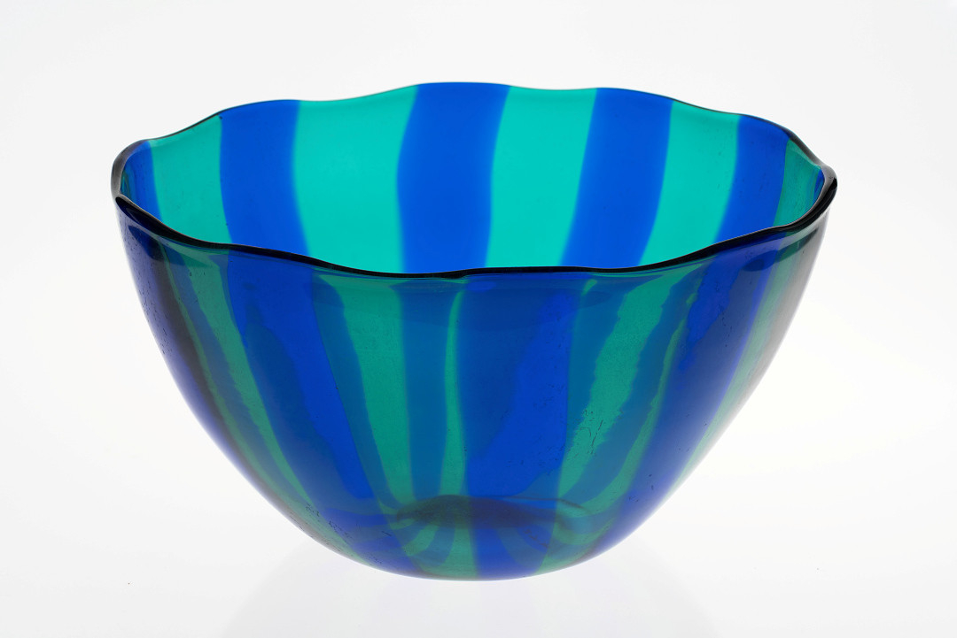 Halvkuleformet bolle i gjennomskinnelig farget glass, dekorert med vertikale striper i grønt og blått på korpus.