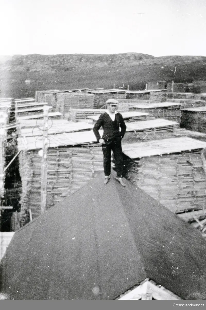 En person står på ett tak framfor materialstabler på sagbruket Pasvik Timber. 