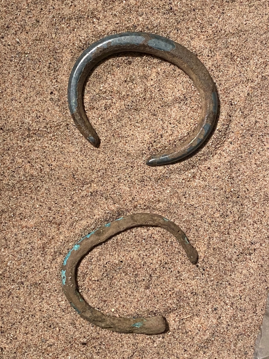 Oregelbundet ovalt formad, ej sluten armring av brons. Tillverkad av en 17 cm lång bronsten som smalnar av vid ändarna. Ett mindre, borrat, hål vid den tjockare delen efter metallanalys. Sammanhör med M 67649-61 (under i bild)