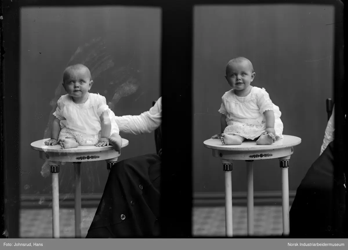 Dobbeltportrett. Baby sittende på bord. Kvinne sittende delvis synlig på siden.