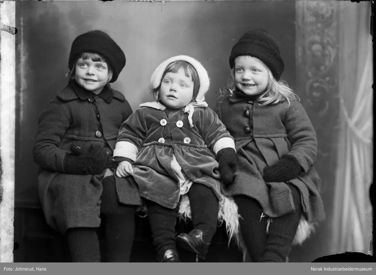 Portrett. Tre barn i yttertøy sittende i fotostudio.