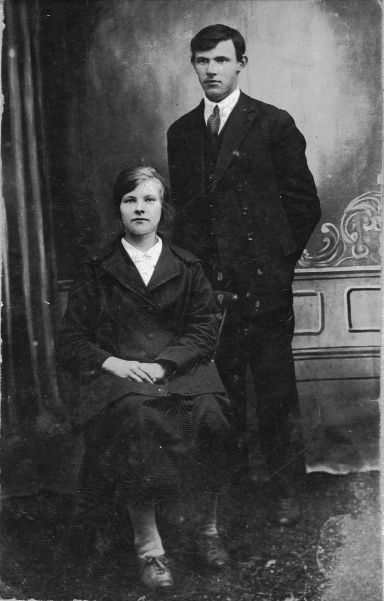 Studioportrett av ung kvinne sittende i en stol og en ung mann stående bak.