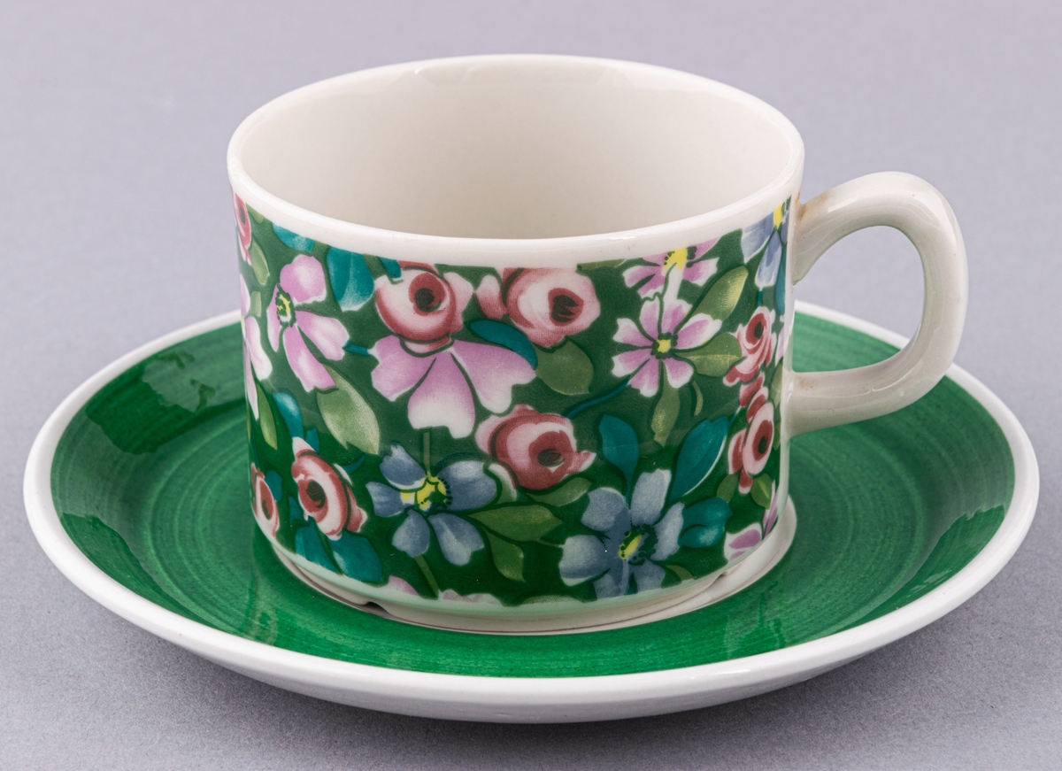 Kaffekopp med fat, i flintgods. Modell EH, dekor Flox (grön). Vit glasyr med grönt blommönster, grönt fat. Skapad av Helmer Ringström för Gefle Porslinsfabrik 1973.