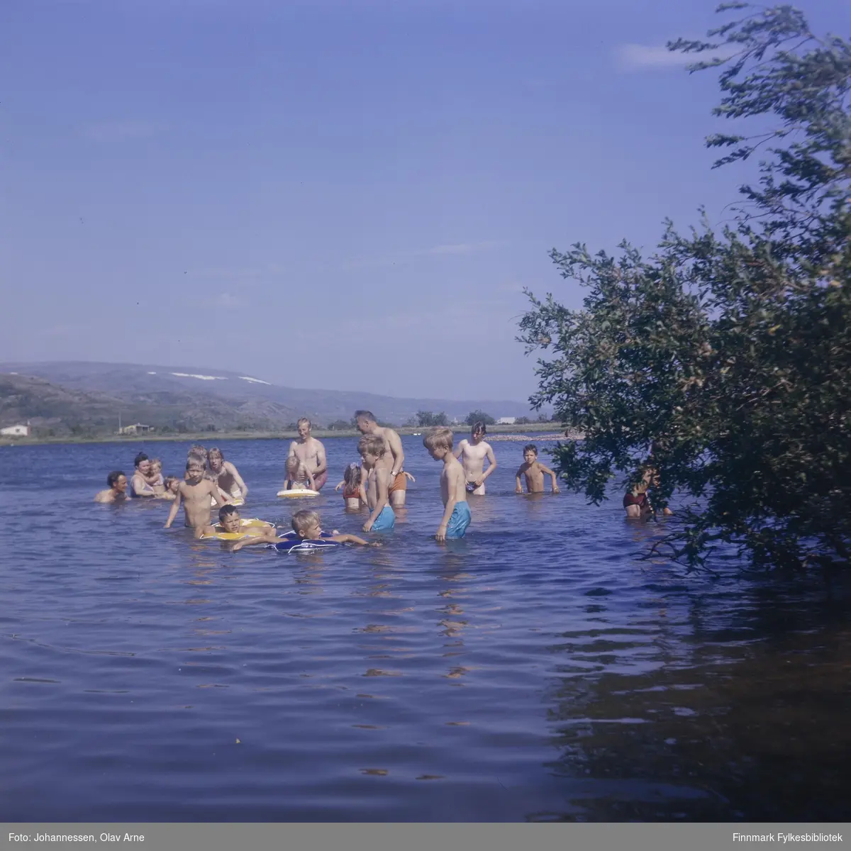 Foto av barn og voksne som bader i Jovatn i Båtsfjord

Mann helt til venstre er Eilif, og kvinnen med siden var Astrid Eriksen med datter (Irene eller Inger, usikker identifisering)

Foto trolig tatt på 1960/70-tallet