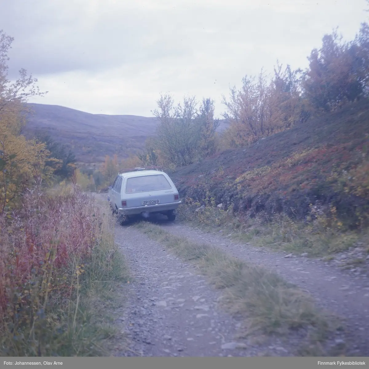 Bil står parkert på siden av grusvei, muligens i Syltefjorddalen (Finnmark)

Bilen tilhørte maleren Olav Johannessen og er en Opel Rekord 

Skiltnummer: ZP 12269
