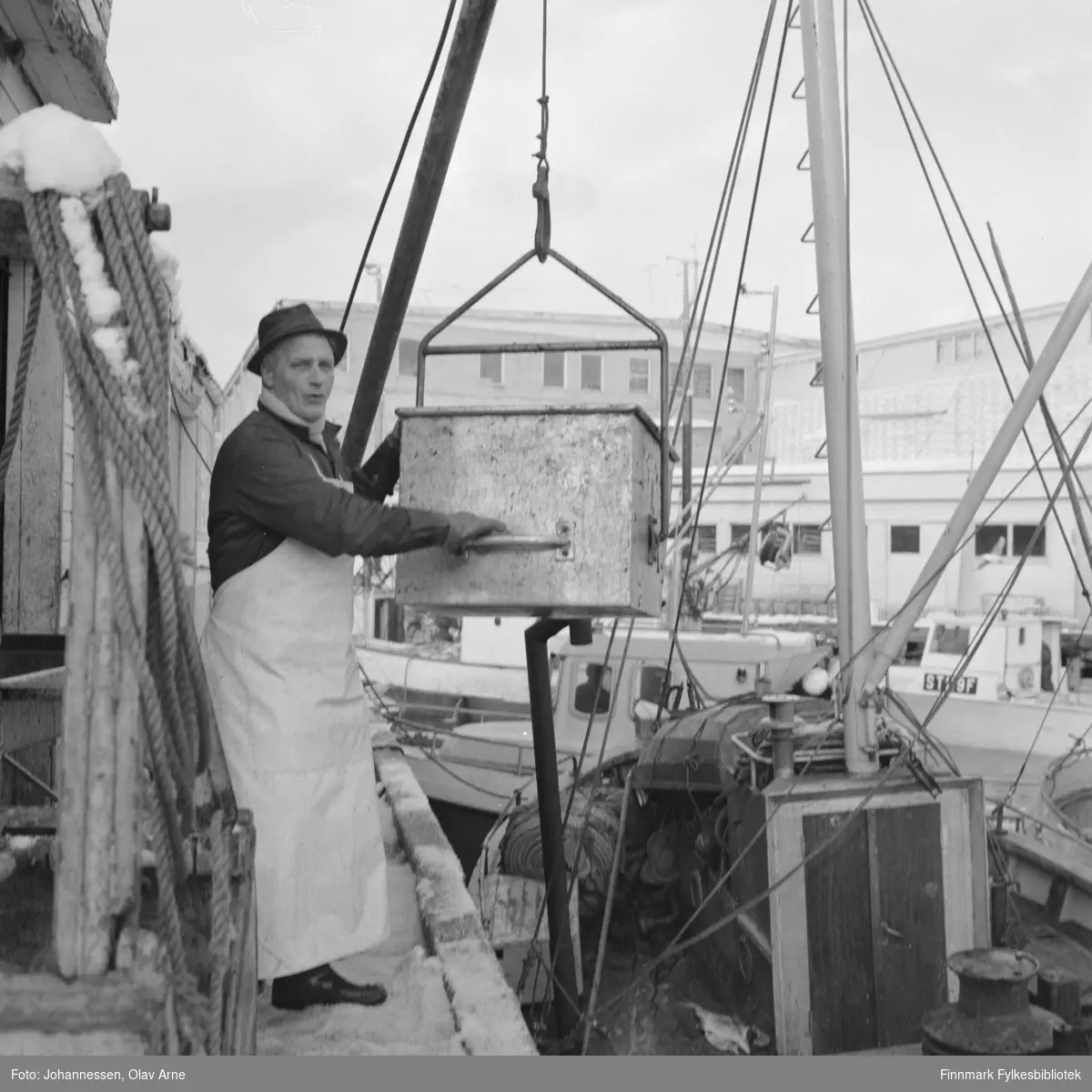 Foto av mann som tar i mot fisk på Kristian Voie kaien med Nils H. Nilsens fiskebruk  i bakgrunnen.

Trolig Peter Johnsen som er avbildet 