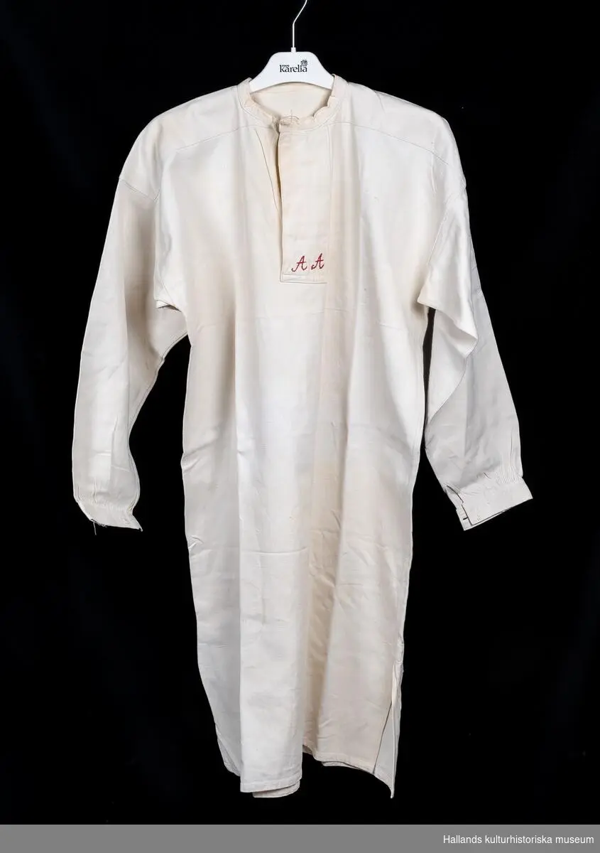 Skjorta av kypertvävd bomull, maskinvävd, lång ärm, sprund med slå framtill. Märkt "AA" med rött bomullsgarn framtill.