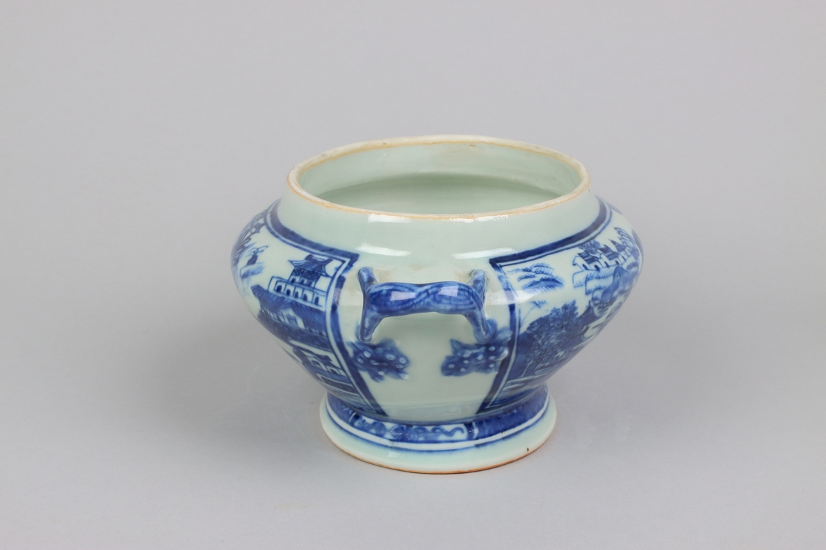 Oval, lobed bowl with angular handles, supported on a central foot. On the both sides decor of landscape scenes of pagodas, buildings, gardens and waters. Handles in shapes of bent tree branches. On the foot a  dark blue border with rectangular reserves filled with symbols of fortunes. The base of the bowl  with unglazed ring.