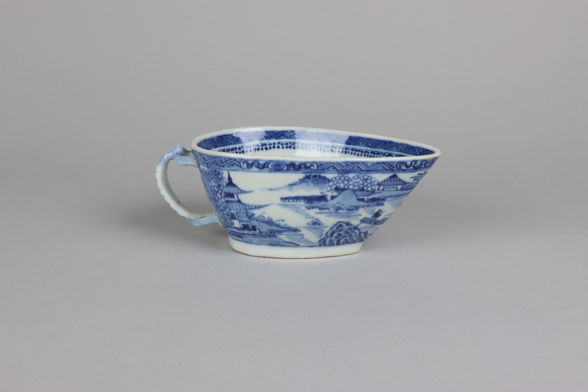 Oval form with a sharp front. On the back a handle in shape of twined branches. Around the edge a border with criss cross pattern and on the sides landscapes scens with pagodas, water and buildings.  The rim decorated with a border with criss cross pattern. Al decorations in blue underglaze. The bottom and the well is undecorated.