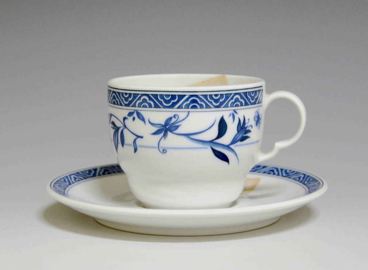 Kaffekopp av porselen med hvit glasur.  Dekorert med blå blomster med en blå bord øverst mot toppranden.
Modell: 2690.2 Roma av Grete Rønning
Dekor: Aurora av Astri Reppe