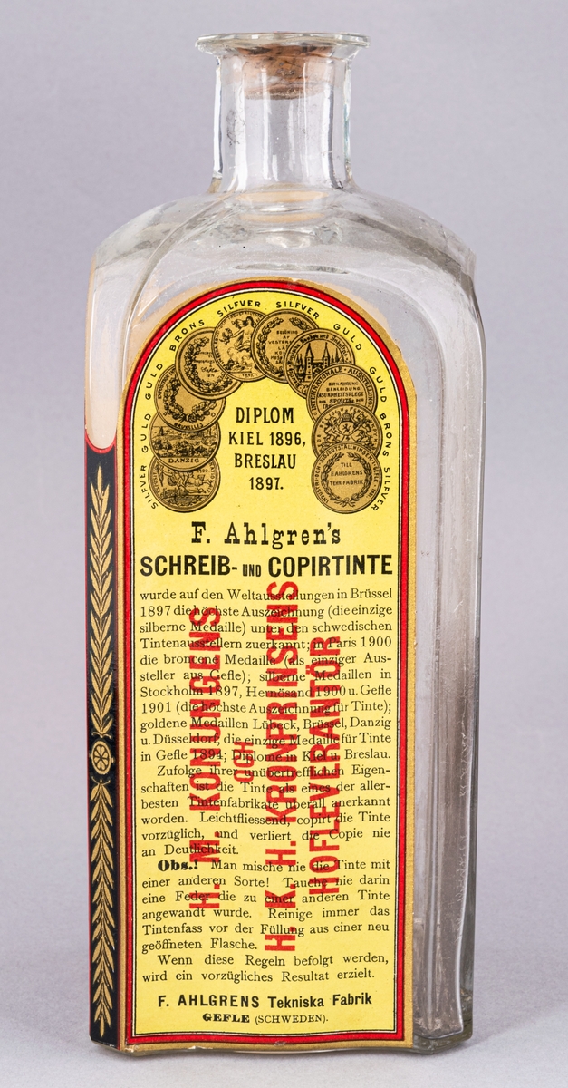 Glasflaska med kork innehållande bläck. Flaskan fyrsidig. Etikett med text "Skrif- & Kopiebläck" på framsidan.
