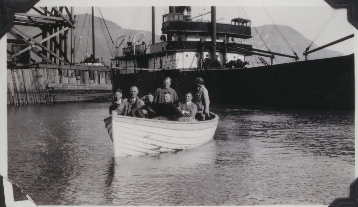 Fotografens far, Knut og Per på besøk. Sju personer i lettbåt foran skip ved gamlekaien.  Fra avfotografert album.