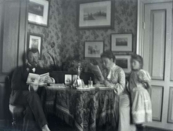 Interiør fra stue. Mann og kvinne sitter ved bord og leser. 