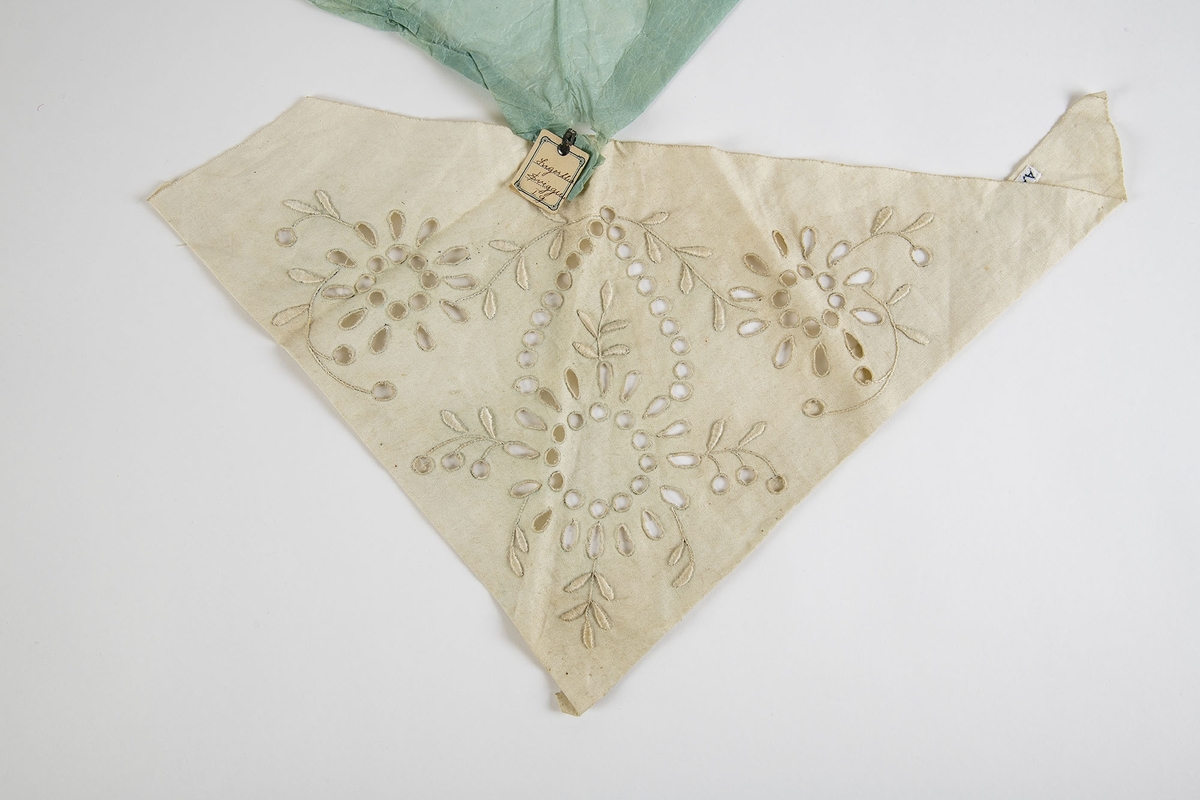 Trekantet stykke lin med et brodert midtmotiv og to "roser" på siden. Montert mot lyseblått silkepapir og med en etikett:  Ingertha Sviggum.