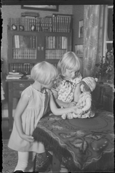 To jenter leker med dukke i stue. Møbel i bakgrunnen med hyl