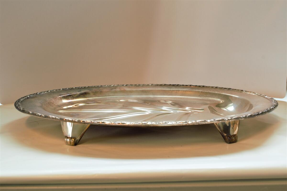 Ovalt serveringsfat av sølvplett, med presset mønster i form av et tre som tjener til å samle opp sausen som renner fra kjøttet. Amerikansk design.