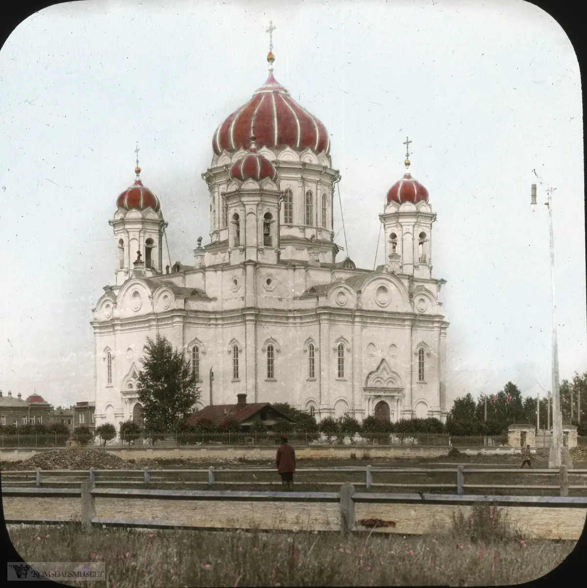 Fra Jonas Lied samlingen., "Church at Tomsk" "Trinity Cathedral" i Tomsk, Russland. Katedralen var den viktigste ortodokse kirken i Tomsk bispedømme i perioden 1900-1930. Den lå på Novosobornaya-plassen i Tomsk. Bygningen ble påbegynt i 1844, men takkuppelen kollapset i 1850 og drepte fire mennesker. Arbeidet ble gjenopptatt i 1858, men ble snart suspendert på grunn av kostnadsoverskridelser og et kjølig klima "for den hellige sak". Det var først i 1885-1889 at kirken ble fullført av byarkitekt V.V. Khabarov. Utsmykningen av katedralen fortsatte til sommeren 1900. I 1930 ble katedralen stengt og i 1934 ble den revet og det istedet anlagt et torg på plassen der kirken stod.