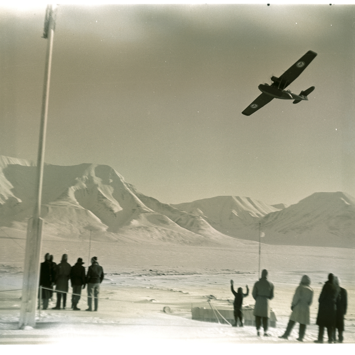 Postflyet dropper postsekker over myra i Longyearbyen 18.mars 1956. Folk som følger med fra bautaen på Skjæringa.