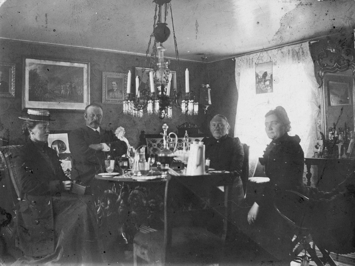 Gruppebilde innendørs. 3 kvinner, 1 mann samlet rundt et dekket bord i en stue.