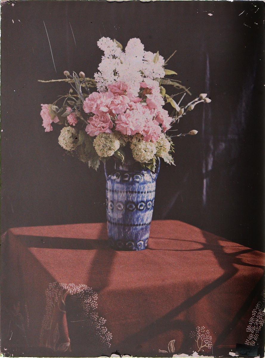 Blå blomstervase med blomster på et bord med en rød duk.