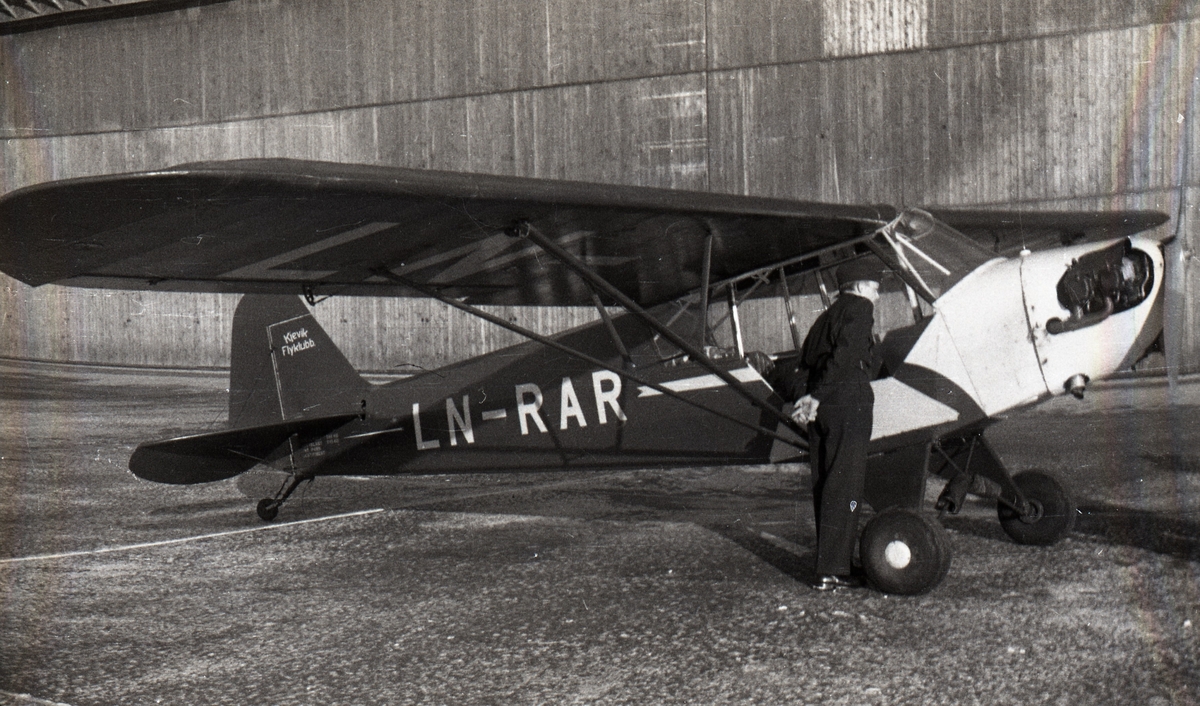 Kjevik Flyklubbs Piper Cub, oppstilt utenfor en av hangarene på Kjevik flyplass.