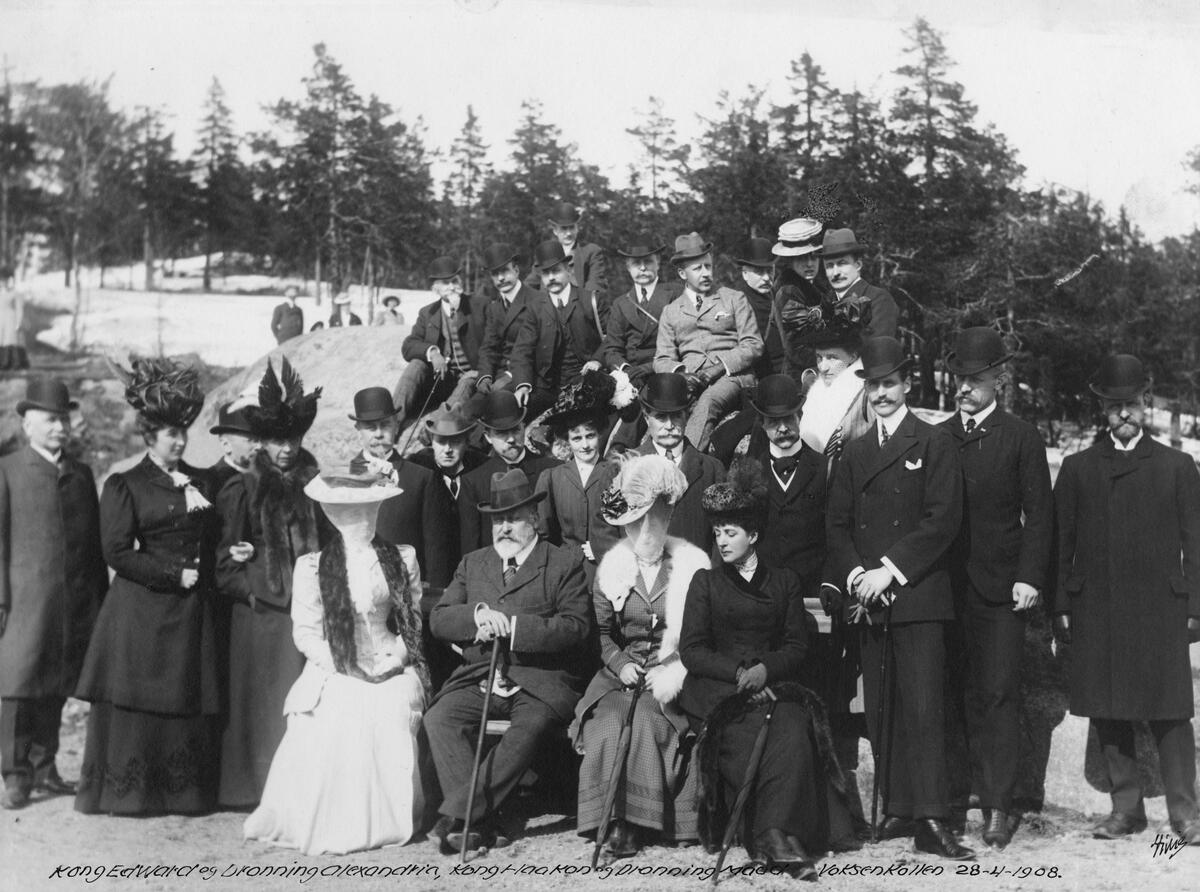 portrett oppstilt gruppe i finklær. ”Kong Edward og Dronning Alexandria, Kong Haakon og Dronning Maud. Voksenkollen 28 – 4 – 1908”. Signert
