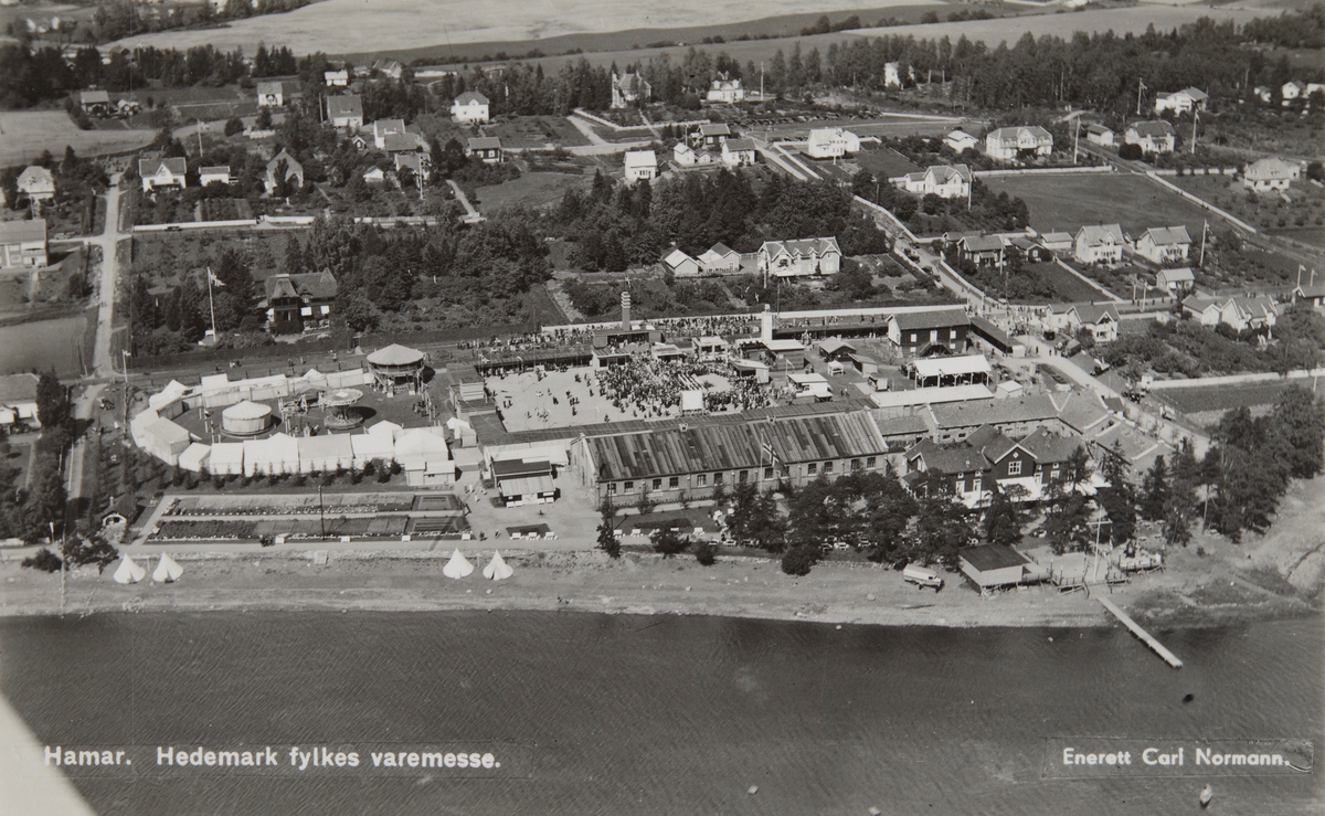 Postkort, Hamar, flyfoto, Hedmark Fylkes Varemesse i 1933 på jordene til Ridehuset, tivoli til venstre, Storhamarstranda, remonteetablissement i Storhamargata 100, vareutstilling, bebyggelse på nedre Storhamar,