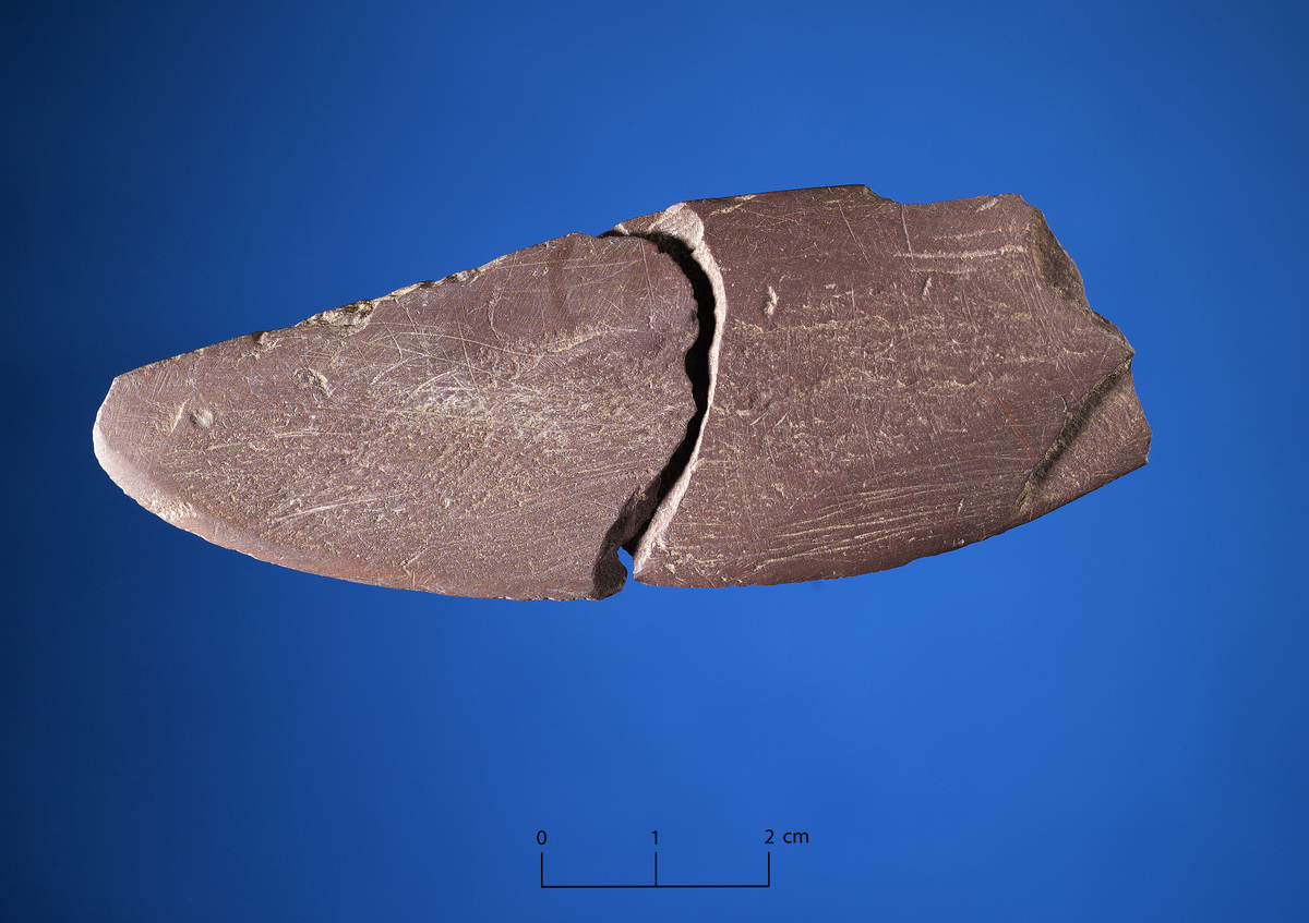 Fragment av enegget skiferkniv. Oddfragment rød skifer. Rett rygglinje med tosidig sliping, buet egglinje. Selve odden mangler. L. 55 mm. st. b. 33 mm, t. 6 mm.