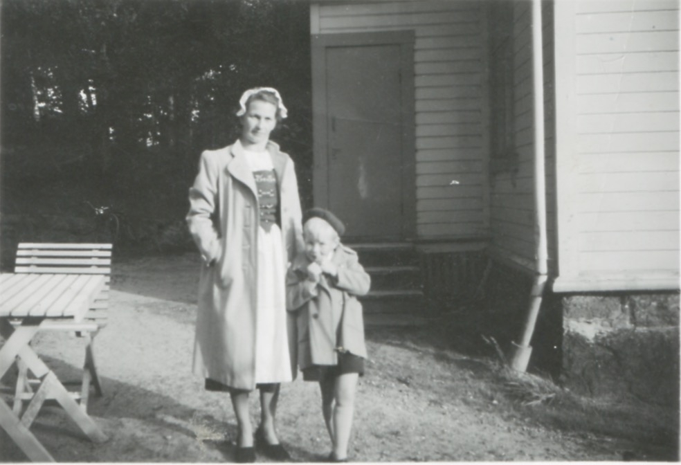 Kållered Stom "Nygård" cirka 1950. Ingeborg Johansson (1901 - 1987, född Gustafsson) och sonen Lars (född 1945) står på gårdsplanen utanför bostaden. Ingeborg bär Bohusdräkten som hon under 1930-talet har sytt tillsammans med väninnor i SLU (Svenska Landsbygdens Ungdom, blev senare CUF).
