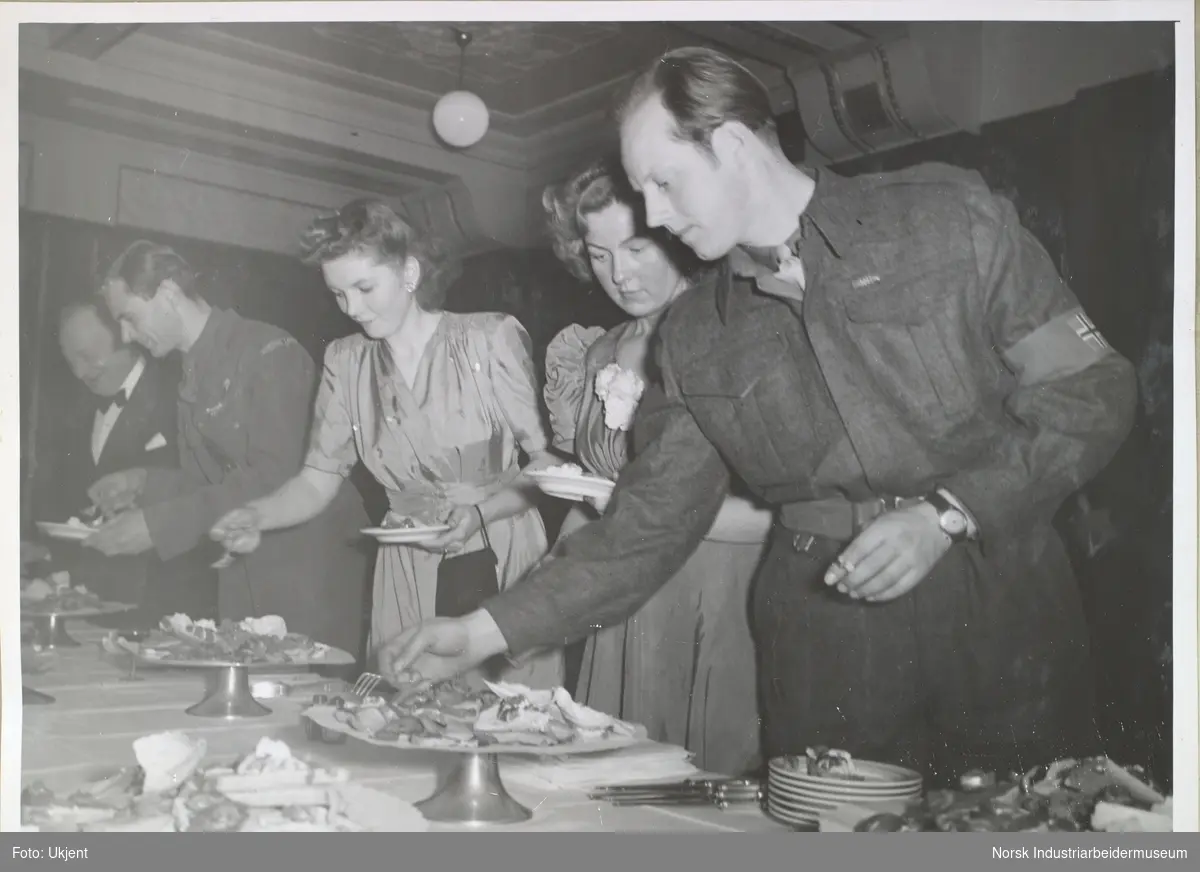Menn og kvinner forsyner seg fra koldtbord. To av mennene, Claus Urbye Helberg og Birger Strømsheim kledd i uniform.