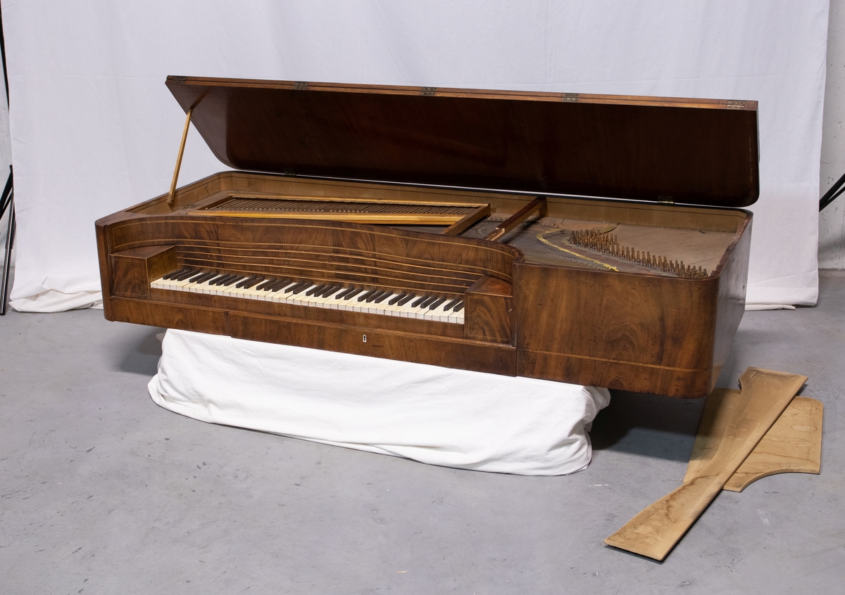 Liggende piano med rektangulær kasse og fire riflede ben. Pianoet har harpeformet pedalstøtte.