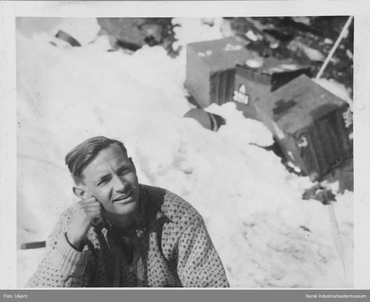 Olav Aarsæther sittende i Tafjordfjella, kasser liggende i snøen bak han.