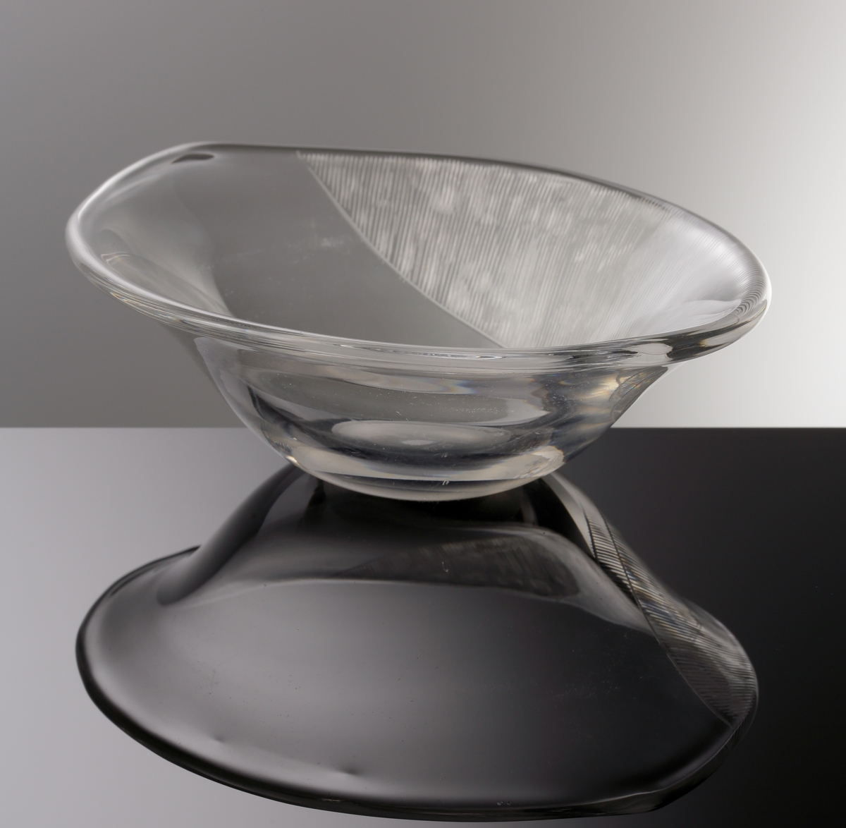 Formgiven av Edvin Öhrström. Oval skål (prov) med yttäckande slipad dekor på skålens ena sida.
