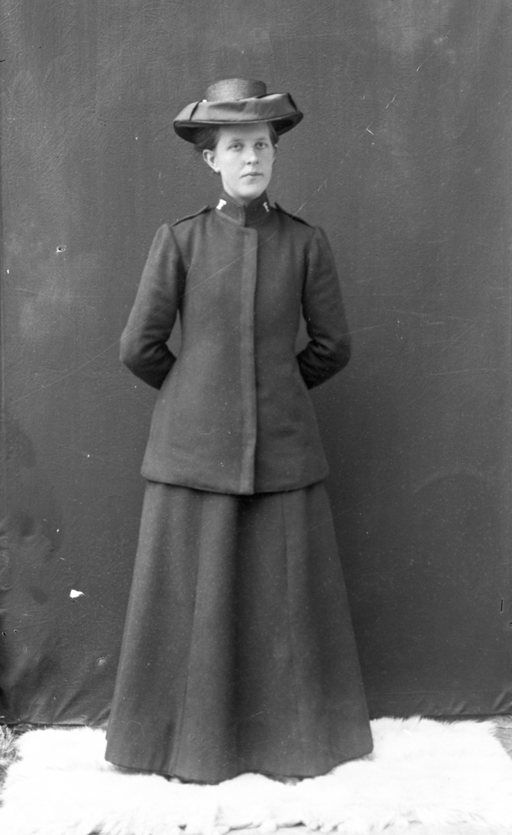 Atelierfoto. Helfigur. En kvinne med hendene på ryggen i uniform fra Frelsesarméen.
