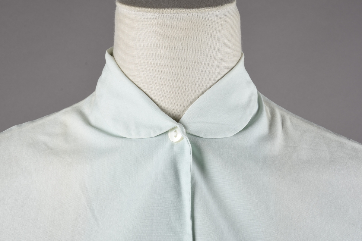 Ermeløs bluse av bomull. Blusen er kneppet i front med fem knapper i plast.