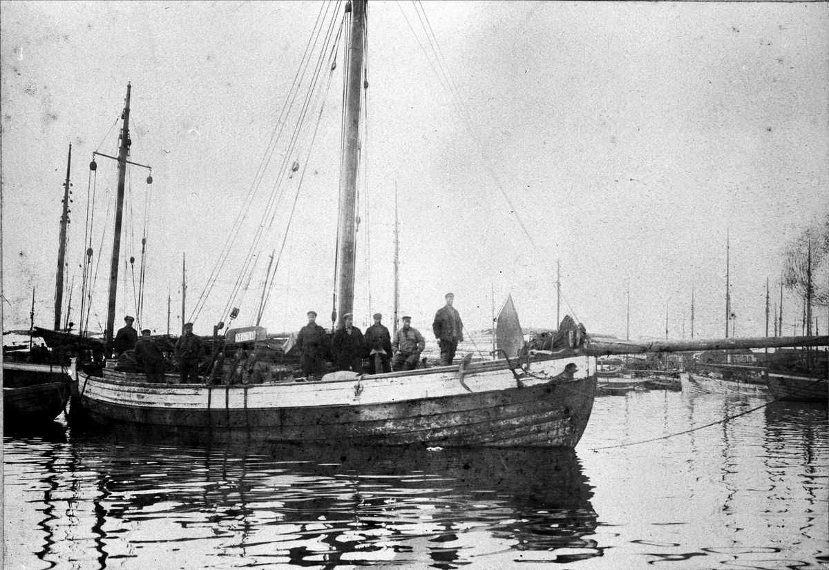 Fiskebåt i havn med mannskapet stående på dekk.