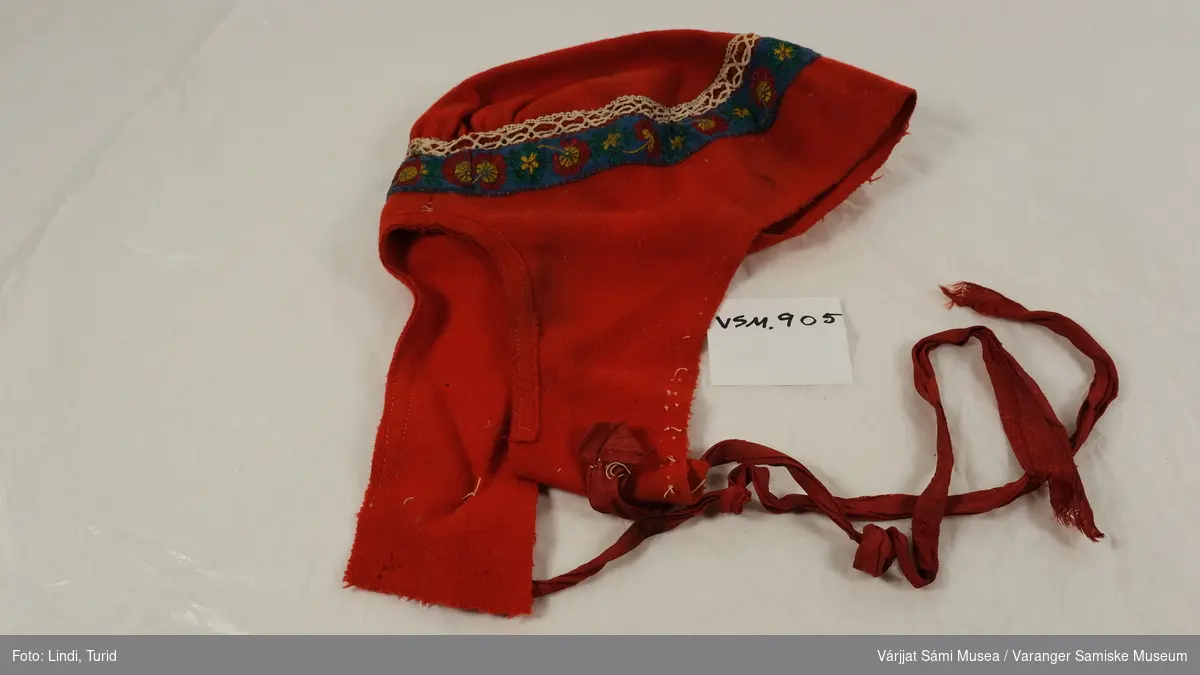 Tradisjonell koftelue til kvinne. Laget av rødt kledestoff med mønsterbånd og knytebånd av silke og bomull.