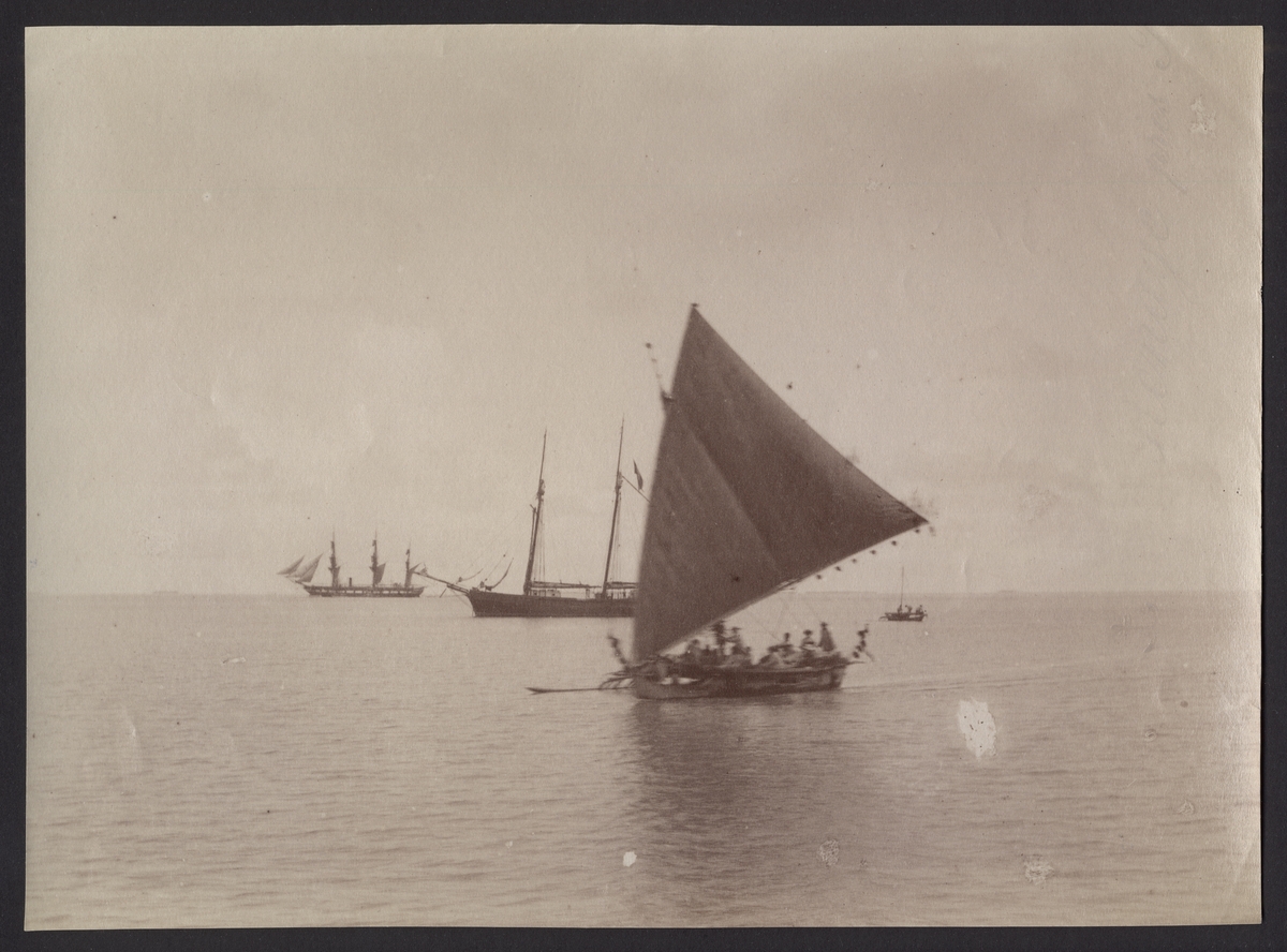 Bilden visar en utriggare kanu seglande på havet. I bakgrunden syns fregatten Vanadis med satta segel. Däremellan befinner skonaren av kung Kabua.