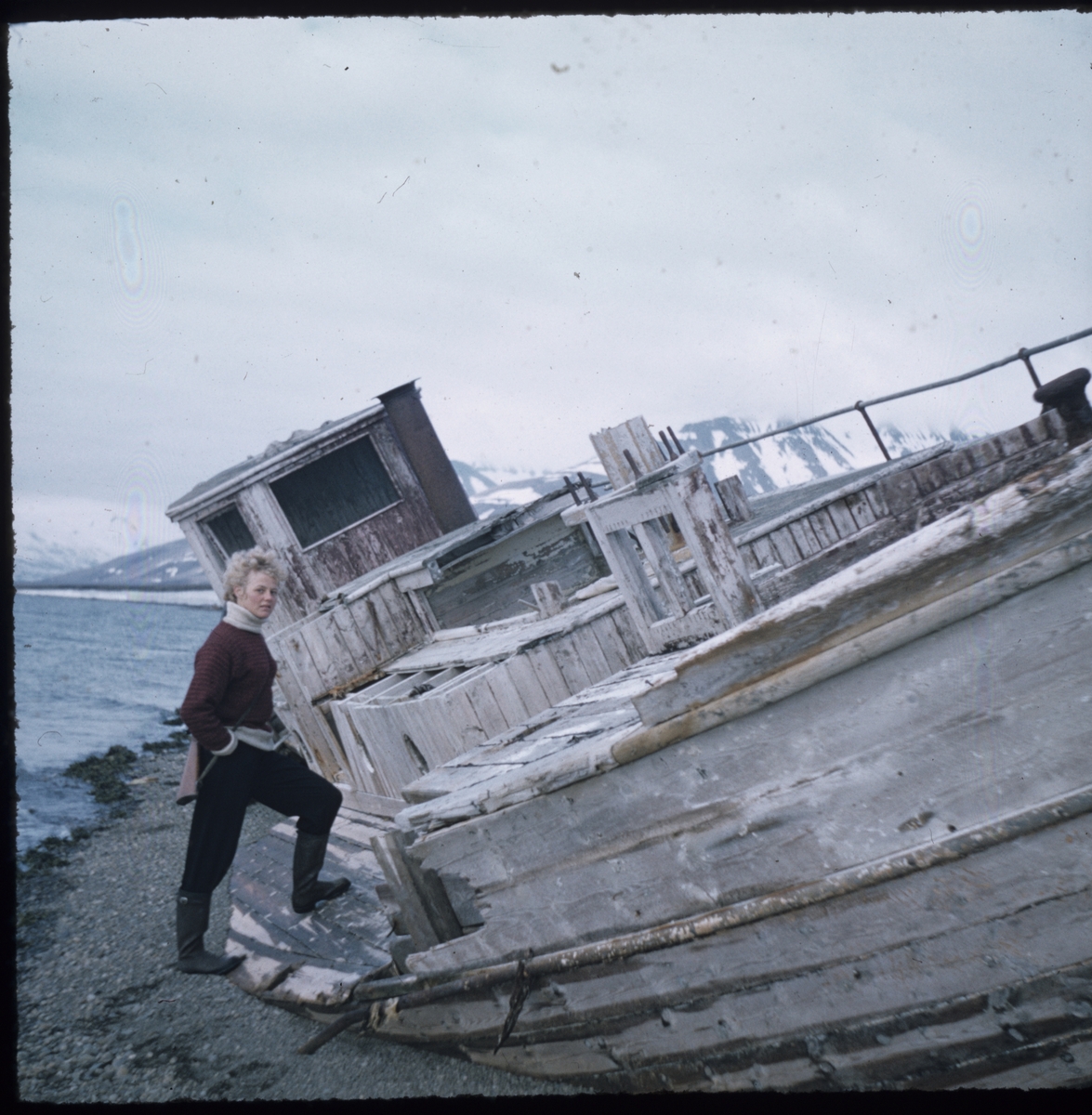 Kvinne foran båtvrak. Foto fra Nils Gunnar Asman Erikson sin samling. Han jobbet som lastesjef på Hotellneset fra 1955 til 1956.