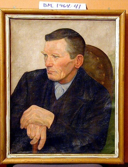 Portrett av en mann, sittende med hendene hvilende på en stokk.
