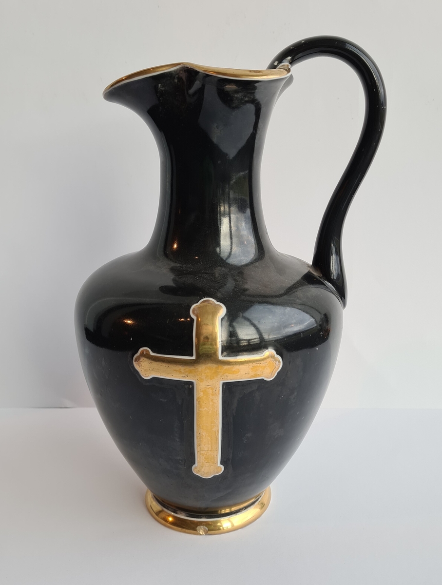 Oinokhoe-formet mugge av porselen med hank. Den er svart med forgylt kors på korpus, rund fot og nebb, samt med hvite konturlinjer.
